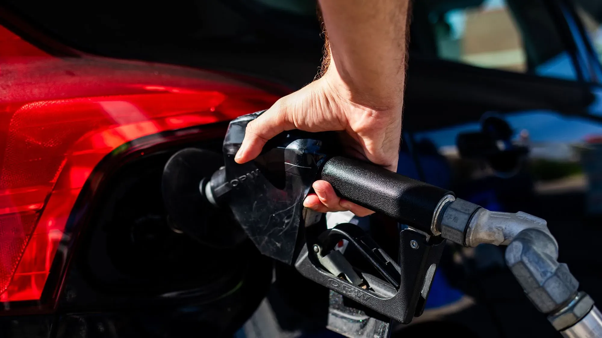 تظهر الصورة شخصًا يملأ خزان وقود سيارة حمراء، مما يعكس تأثير التعريفات الجمركية على تكاليف الطاقة في أمريكا.