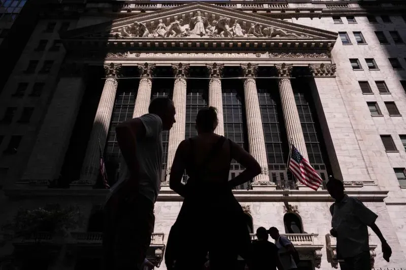 واجهة بورصة نيويورك مع أشخاص يتحدثون في المقدمة، تعكس حالة عدم اليقين في الأسواق المالية بعد تمرير قانون الضرائب.