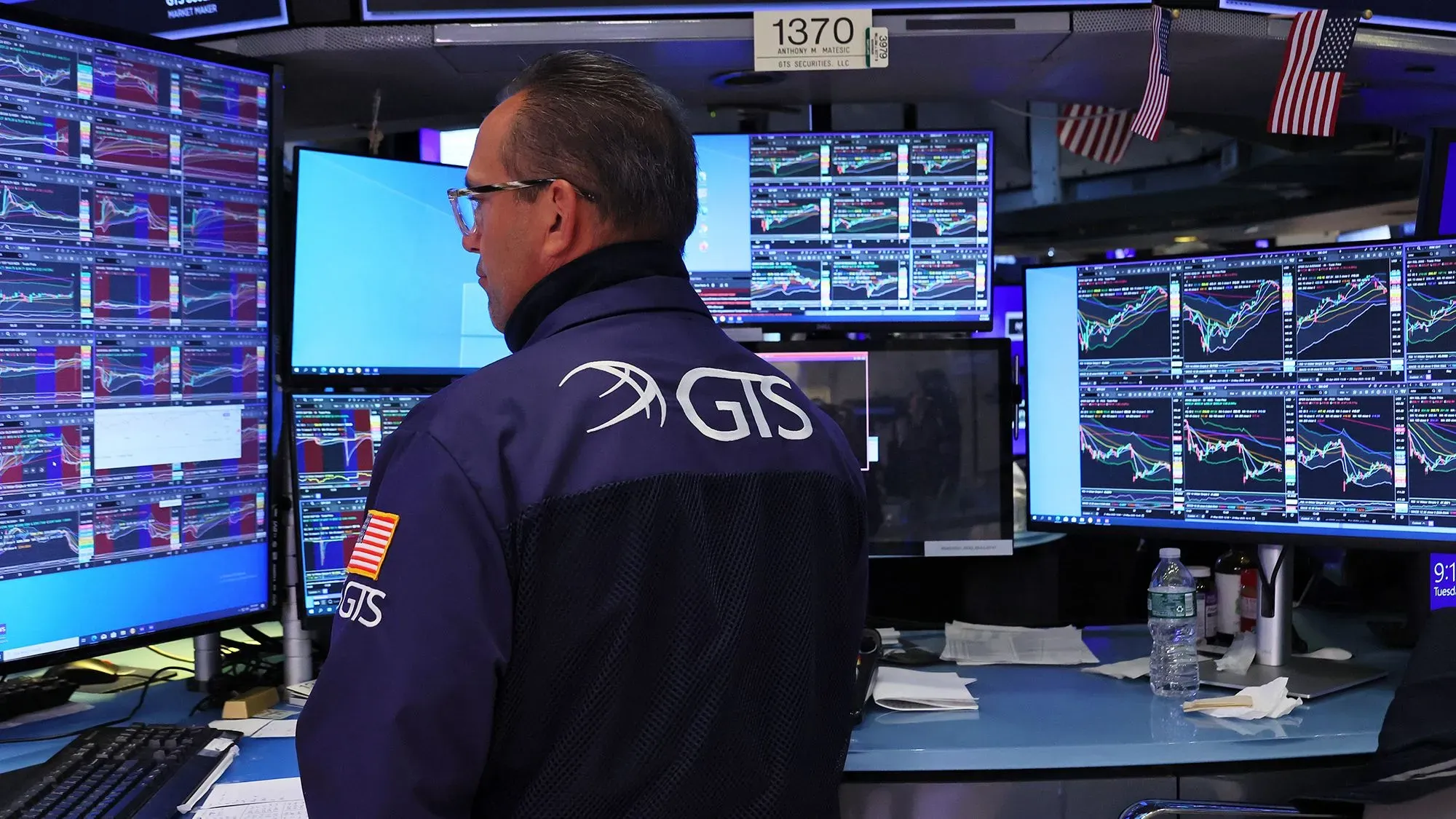 متداول يراقب شاشات متعددة تعرض بيانات السوق والأسهم، مع التركيز على تأثير الحرب التجارية على أسواق المال.