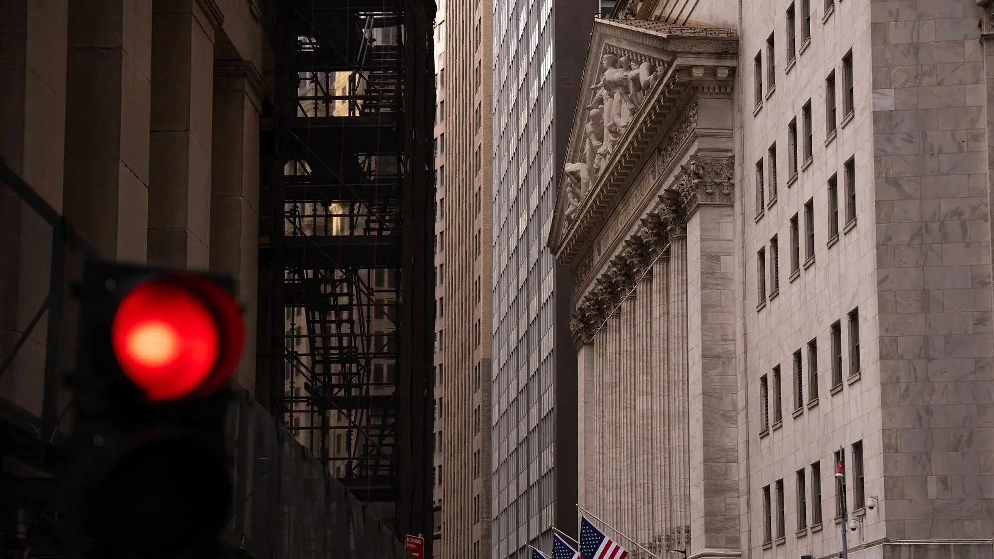 إشارة حمراء أمام مبنى البورصة الأمريكية، مع وجود أعلام أمريكية في الأسفل، تعكس التوترات في الأسواق العالمية وتأثير السياسات التجارية.