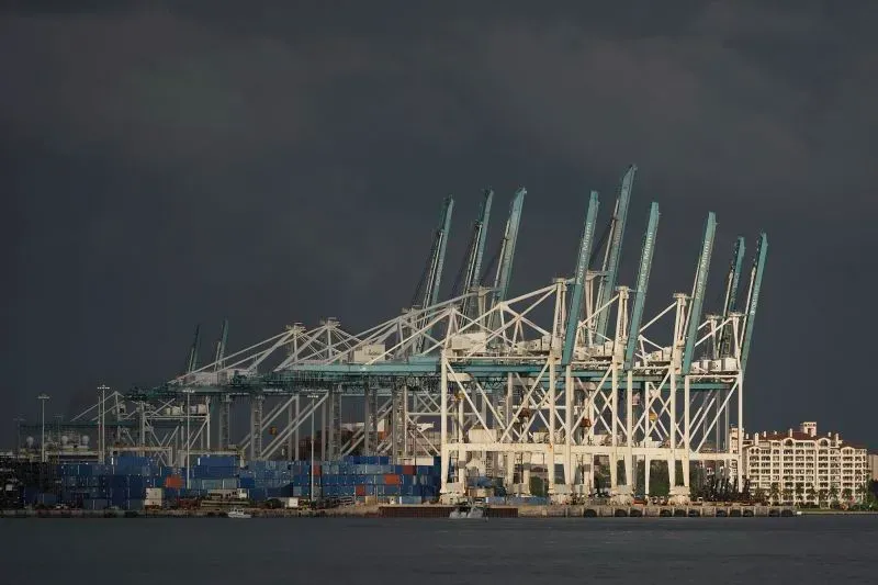 صورة لميناء يحتوي على رافعات ضخمة ومعدات تحميل، مع حاويات شحن ملونة، تعكس تأثير السياسة التجارية على الأسواق العالمية.