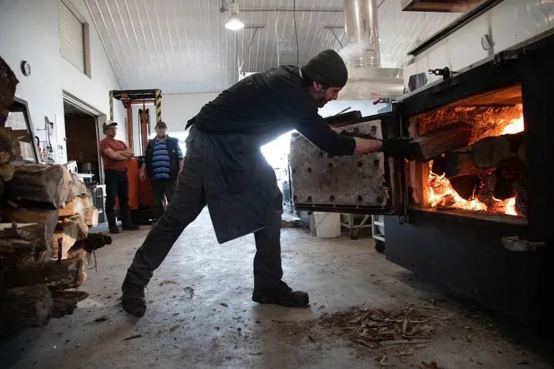 رجل يضع الحطب في فرن لتجهيز شراب القيقب في دار دراي بروك للسكر، حيث يتم إنتاج 4,000 جالون من الشراب وسط غابات القيقب في نيويورك.