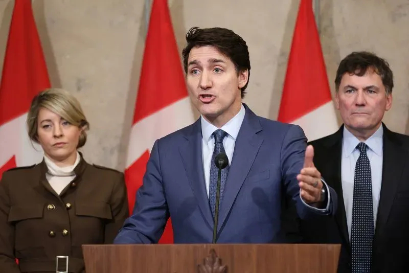 جاستن ترودو يتحدث خلال مؤتمر صحفي، مع وجود علم كندا خلفه، وسط توترات تجارية مع الولايات المتحدة.