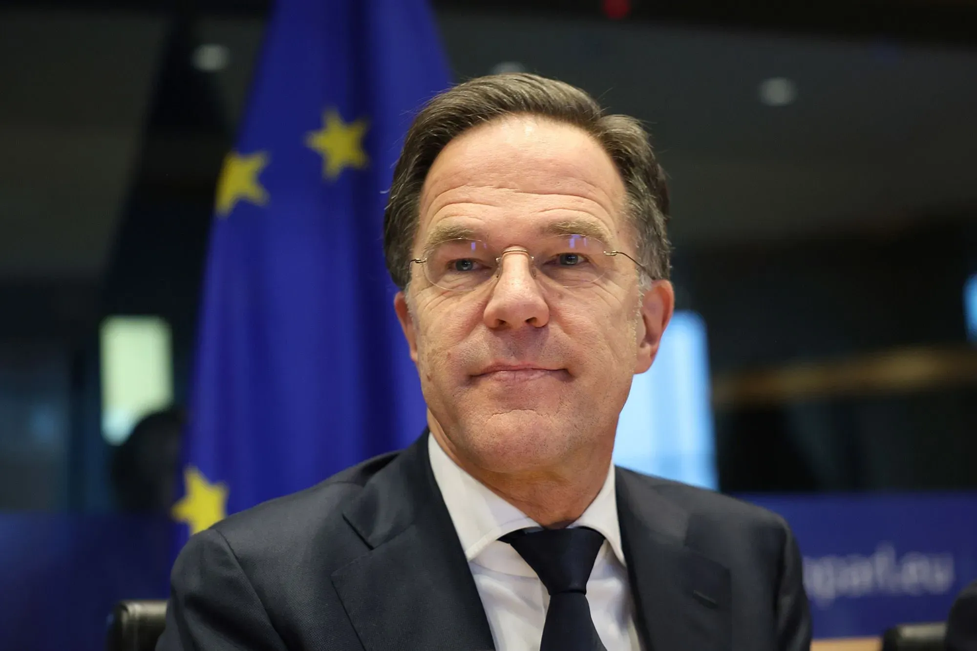 رجل يجلس أمام علم الاتحاد الأوروبي، يعكس الأجواء السياسية في مؤتمر ميونيخ للأمن وتحديات الأمن العالمي.