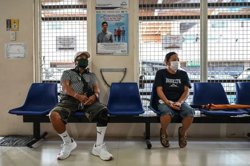 امرأتان ترتديان الكمامات يجلسان في غرفة انتظار، بينما تظهر خلفهما لافتات توعوية عن السل، تعكس تأثير المرض على المجتمع.