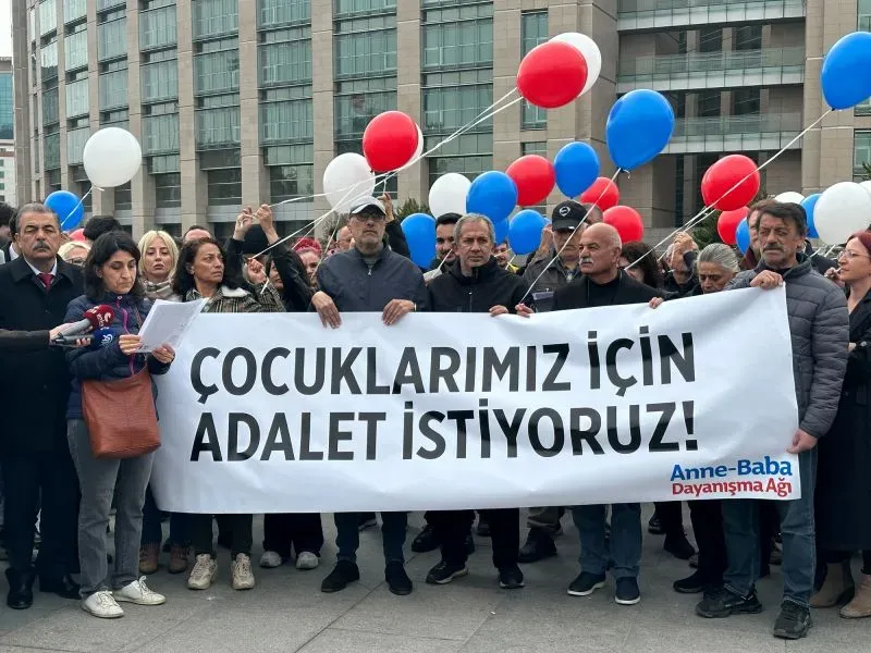 مجموعة من المتظاهرين يحملون لافتة تطالب بالعدالة لأبنائهم، محاطين بالبالونات الحمراء والزرقاء، أمام قصر العدل في إسطنبول.