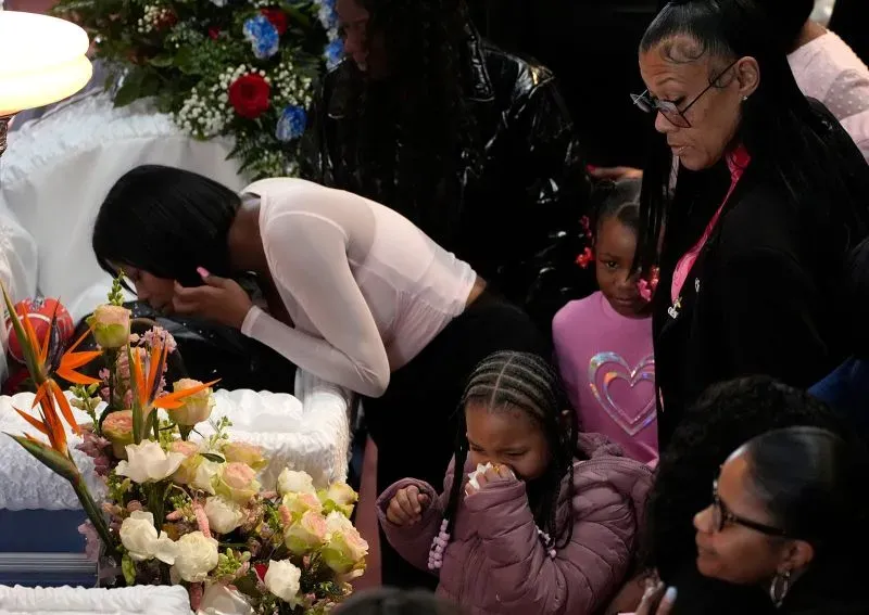 تظهر الصورة عائلة وأصدقاء يتجمعون في جنازة طفلين من ديترويت، مع أجواء حزينة وزهور تزيّن النعش.