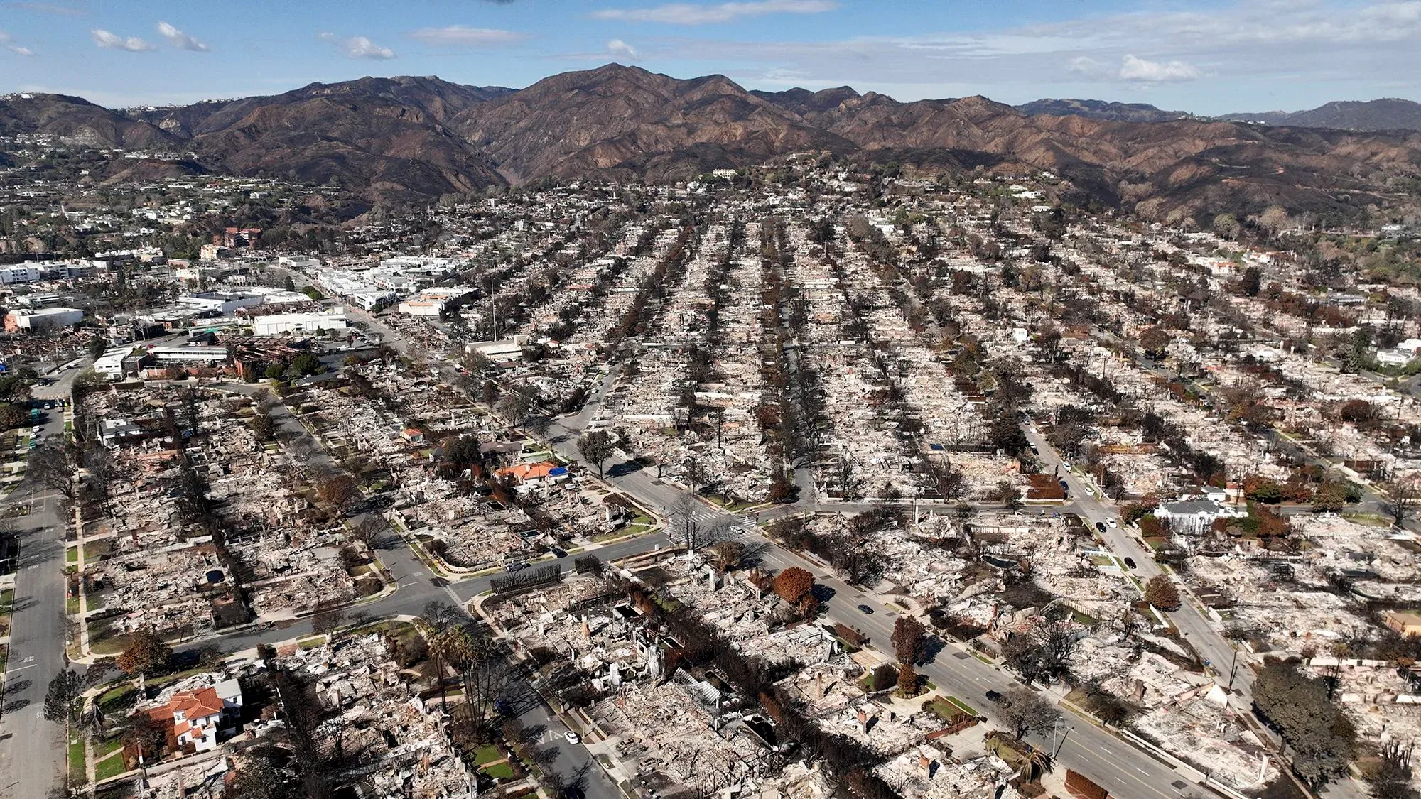 مشهد جوي لمدينة مدمرة بفعل الحرائق، يظهر المنازل المحترقة والأرض القاحلة، مما يعكس تأثير التغير المناخي على المجتمعات.