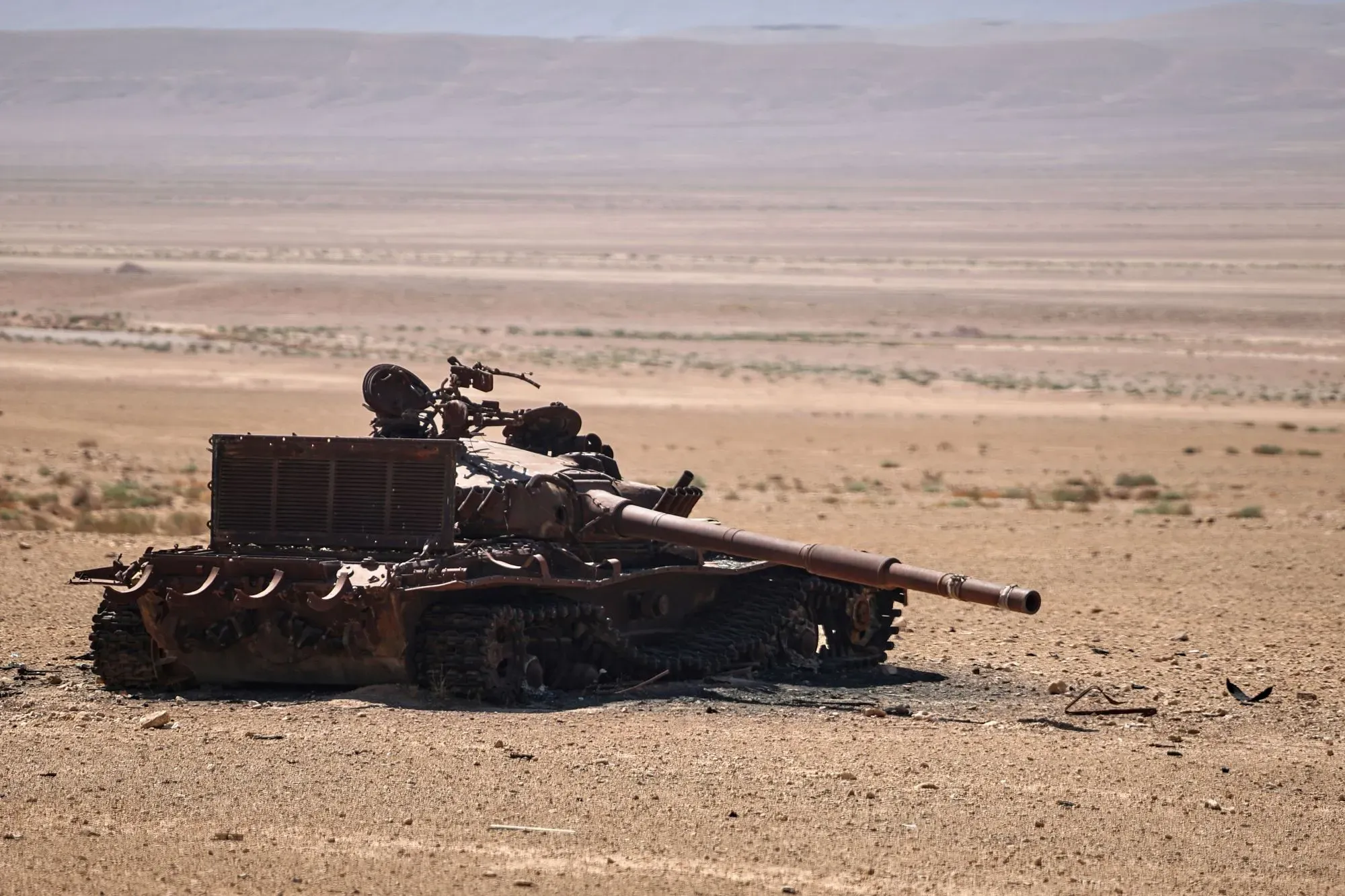 دبابة مدمرة في منطقة صحراوية بسوريا، تعكس آثار الصراع المستمر، مع التركيز على الأوضاع الأمنية والعمليات العسكرية ضد تنظيم داعش.