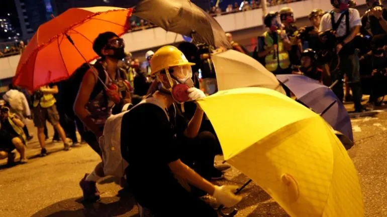 محتجون في هونغ كونغ يحملون مظلات ملونة ويستخدمونها كدرع أثناء مظاهرة، تعبيرًا عن دعمهم للديمقراطية في مواجهة القمع.