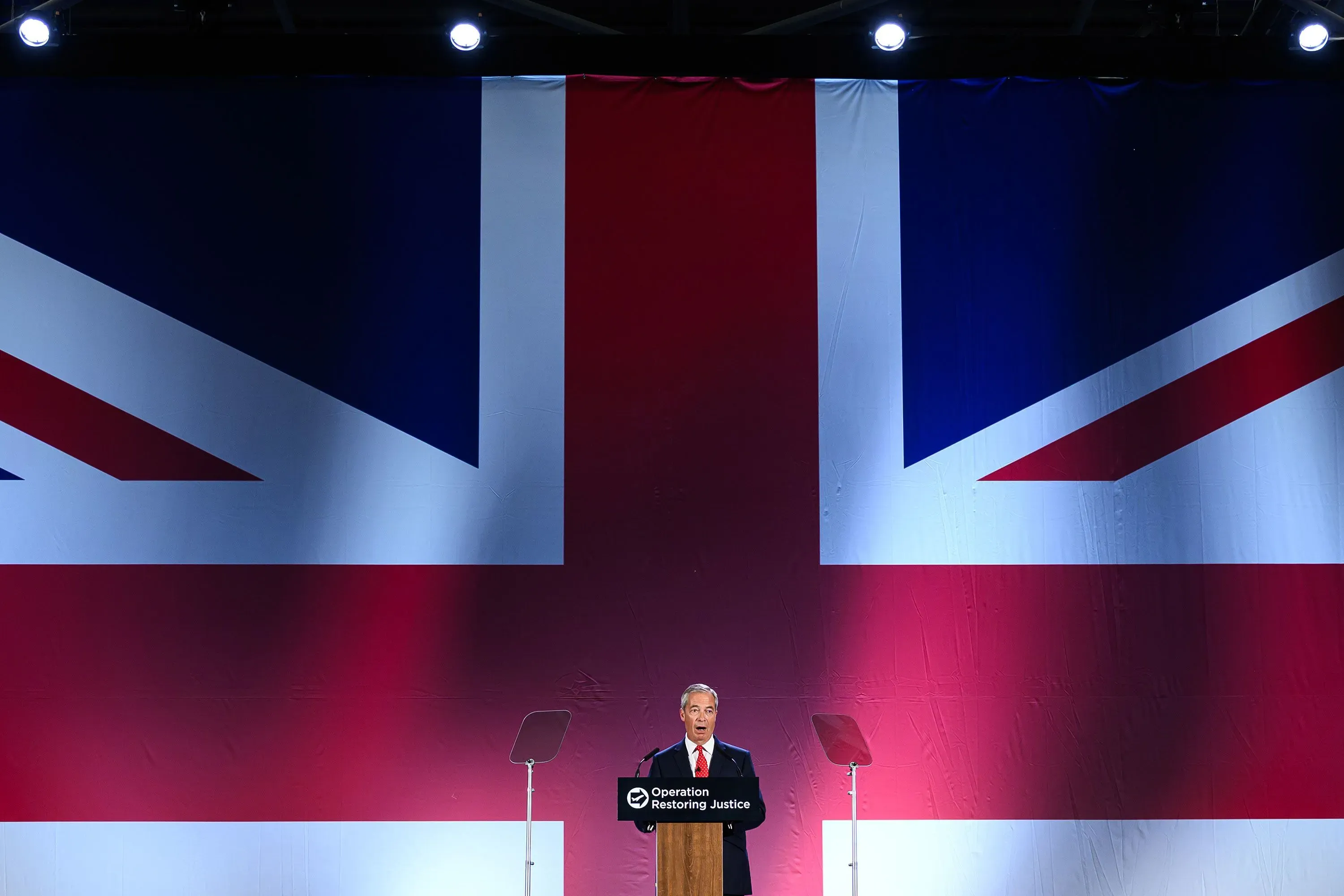 نايجل فاراج يتحدث في مؤتمر صحفي أمام علم المملكة المتحدة، حيث يعلن عن خطط جديدة للهجرة تشمل ترحيل طالبي اللجوء.