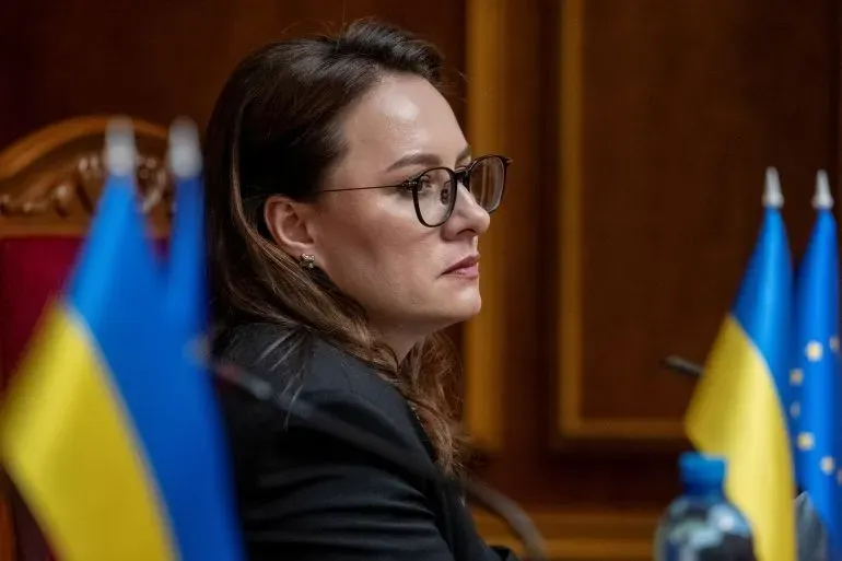 يوليا سفريدينكو، رئيسة وزراء أوكرانيا الجديدة، تجلس بجانب أعلام أوكرانيا والاتحاد الأوروبي، معبرة عن التزامها بتحقيق نتائج إيجابية في البلاد.