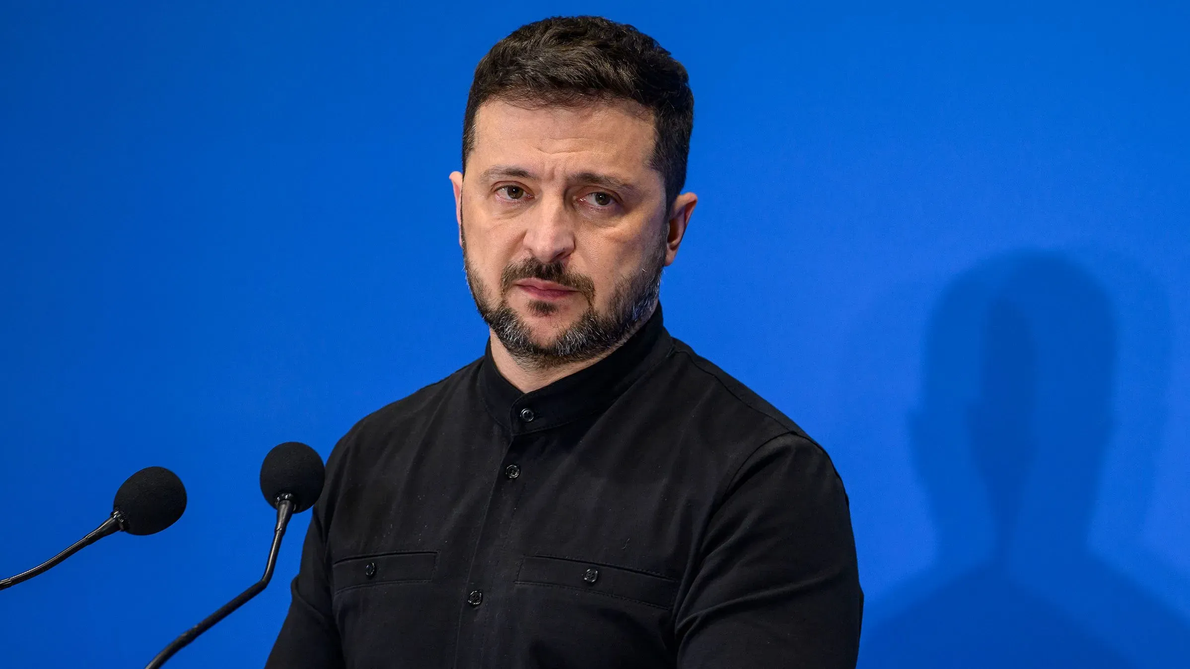 الرئيس الأوكراني فولوديمير زيلينسكي يتحدث خلال مؤتمر صحفي، مع خلفية زرقاء، مع التركيز على دعوته لعقد اجتماع مع روسيا لوقف إطلاق النار.