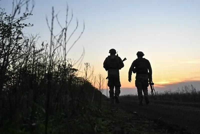 جنود أوكرانيون يسيرون على طريق في وقت الغروب، يحملون أسلحتهم، وسط مشهد يعكس التوترات العسكرية في الصراع الحالي.