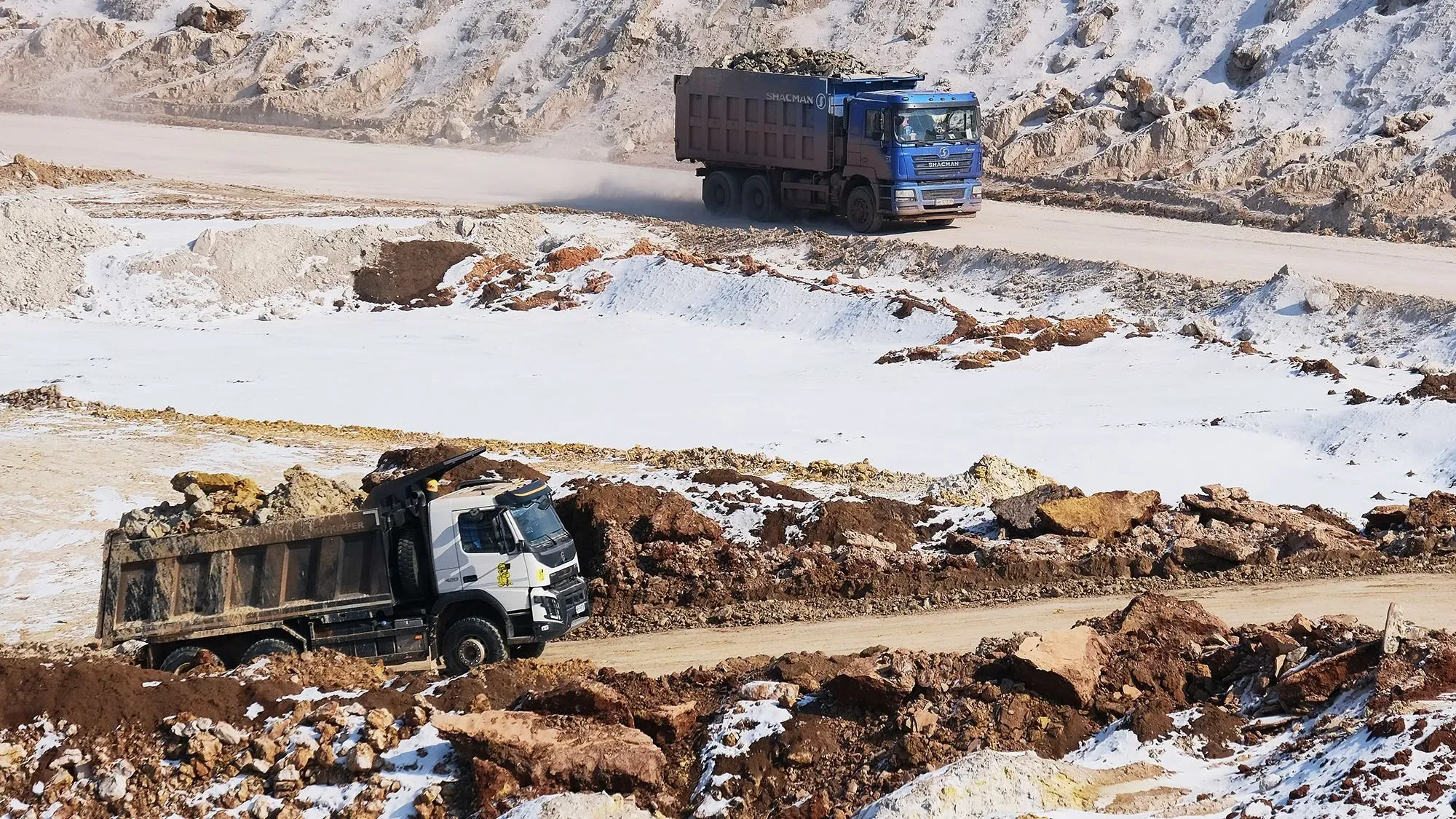 شاحنات نقل كبيرة تعمل في موقع تعدين، محملة بالصخور والمعادن في منطقة ثلجية، تعكس جهود أوكرانيا لتعزيز مواردها الطبيعية.