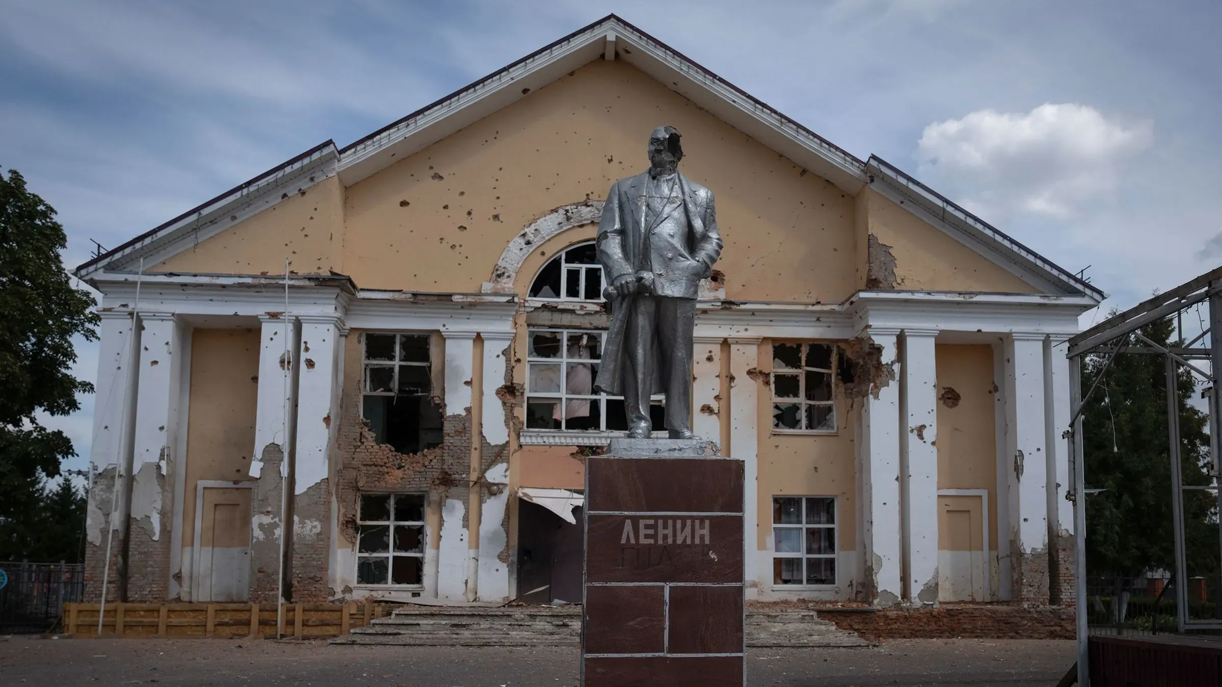 تمثال لفلاديمير لينين أمام مبنى مدمر في بلدة سودزها، يظهر آثار الحرب مع جدران متصدعة ونوافذ مكسورة.