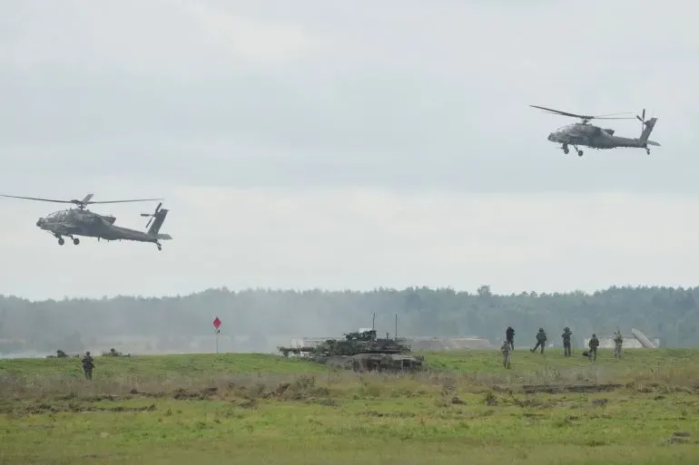 تظهر الصورة مروحيتين عسكريتين تحلقان فوق مجموعة من الجنود والدبابات في منطقة تدريب، مما يعكس التعاون العسكري بين أوكرانيا وبولندا.