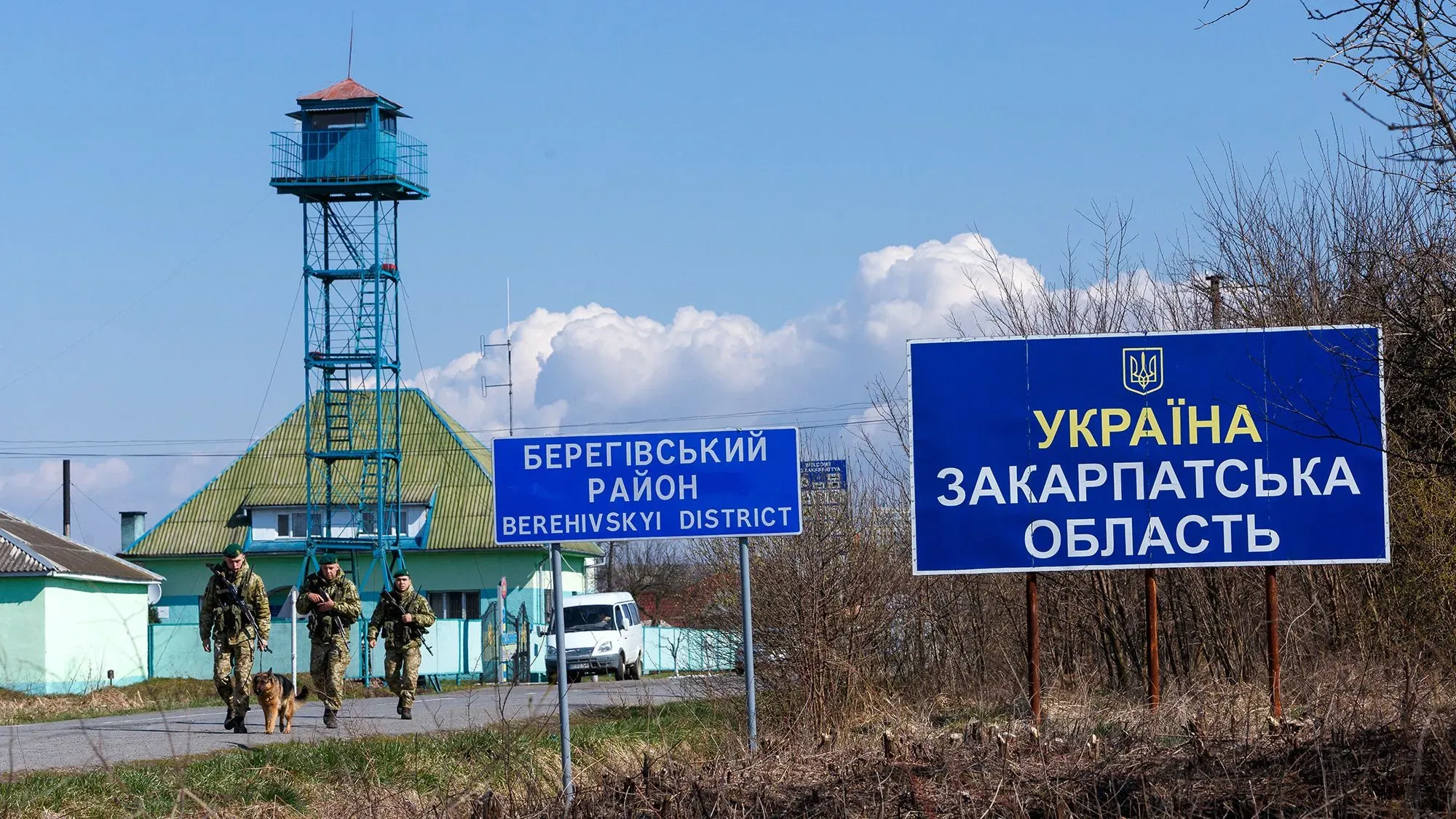 جنود أوكرانيون يسيرون بالقرب من لافتة تشير إلى منطقة زاكارباتيا، مع برج مراقبة في الخلفية، في سياق التوترات الجيوسياسية مع المجر.