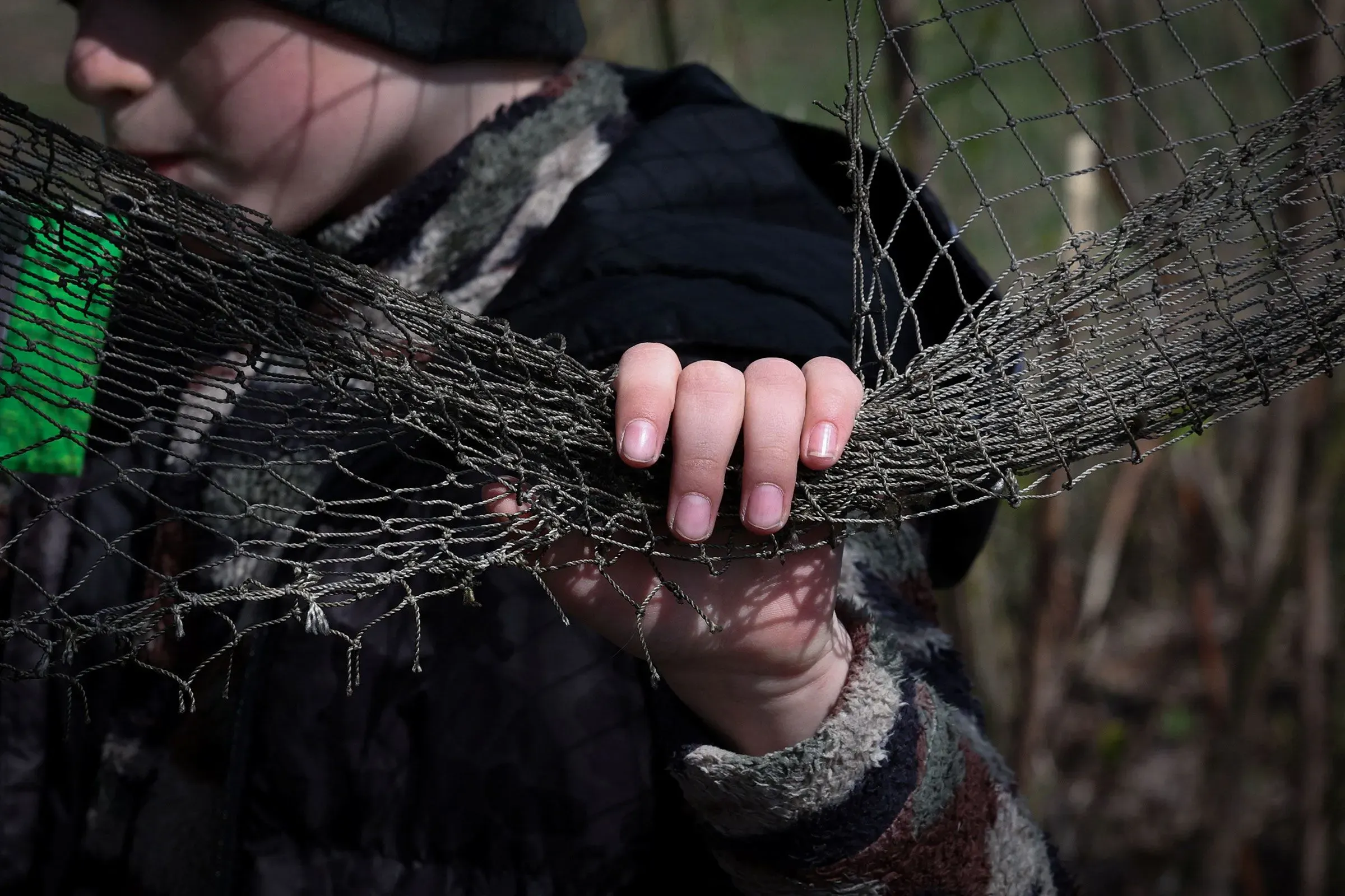 يد تحمل شبكة صيد قديمة، بينما يظهر في الخلفية طفل يرتدي ملابس داكنة، تعكس مشهد الحياة تحت تأثير الحرب في أوكرانيا.