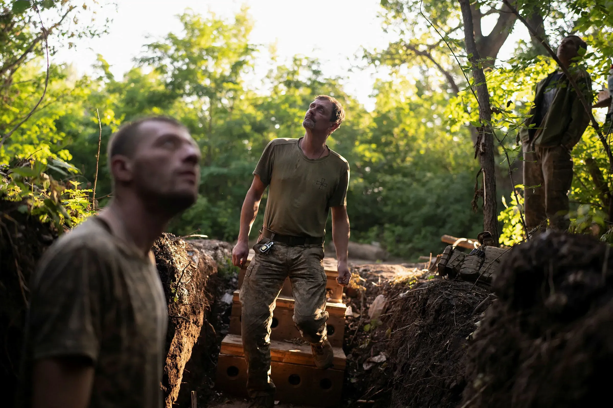 جنود أوكرانيون في خندق، يتطلعون إلى السماء وسط غطاء نباتي كثيف، في سياق حرب الطائرات بدون طيار المتزايدة.