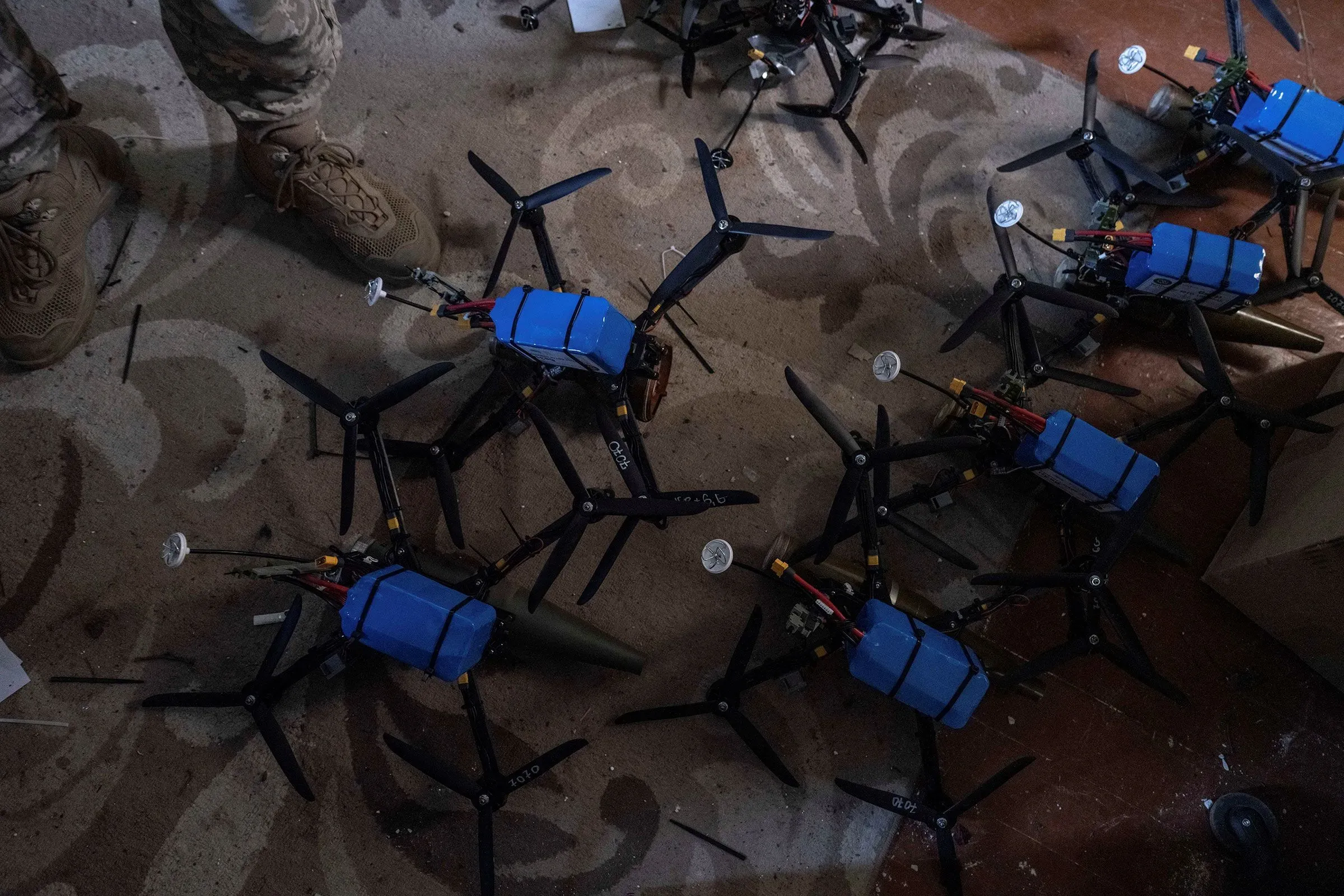 طائرات مسيرة صغيرة مع معدات زرقاء، ملقاة على الأرض، تمثل التكنولوجيا المستخدمة في الصراع الأوكراني الروسي، وسط أجواء الحرب.