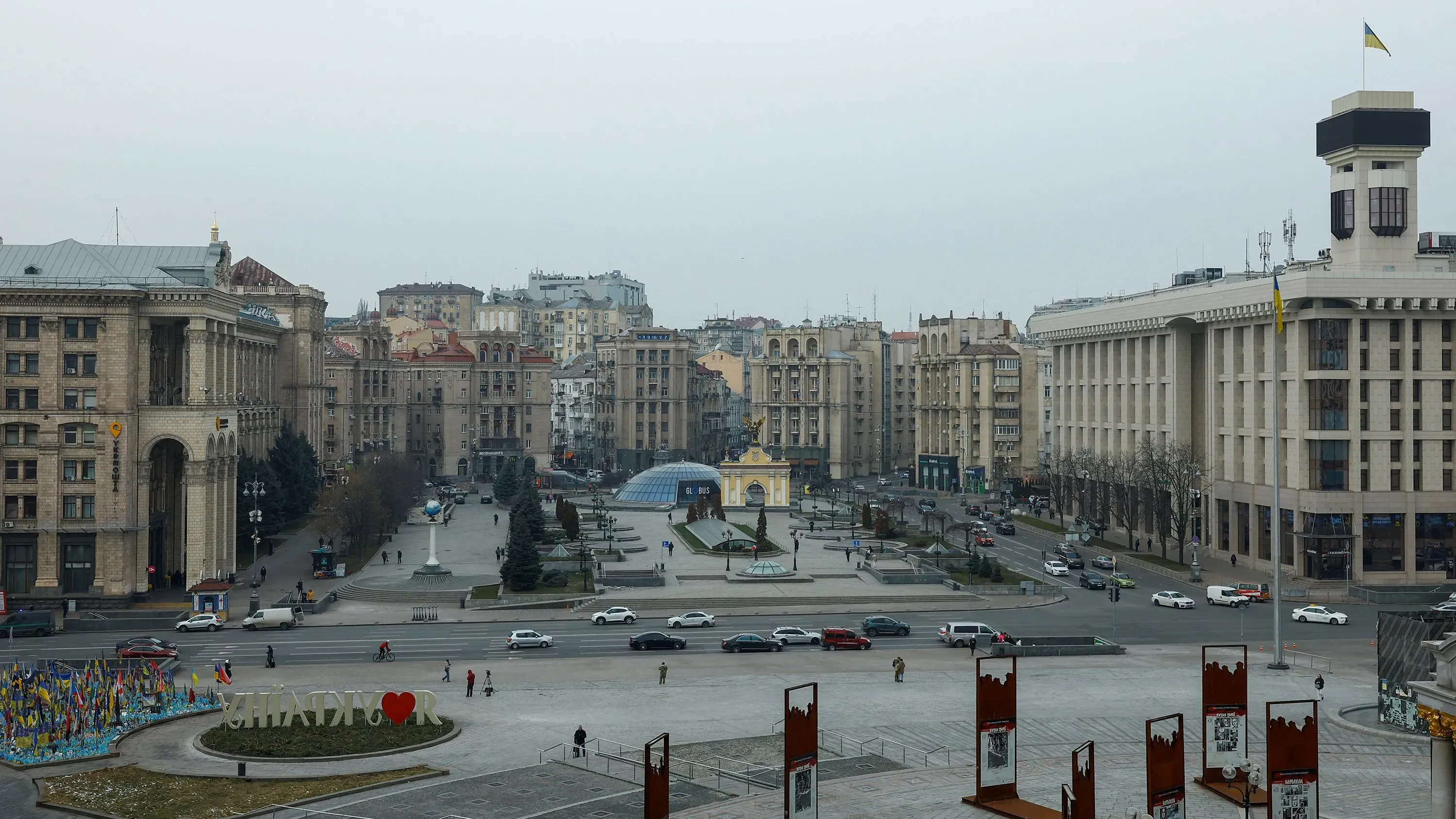 ساحة ميدان الاستقلال في كييف، تظهر المباني التاريخية والسيارات والأعلام الأوكرانية، تعكس الوضع الحالي في أوكرانيا تحت الاحتلال.