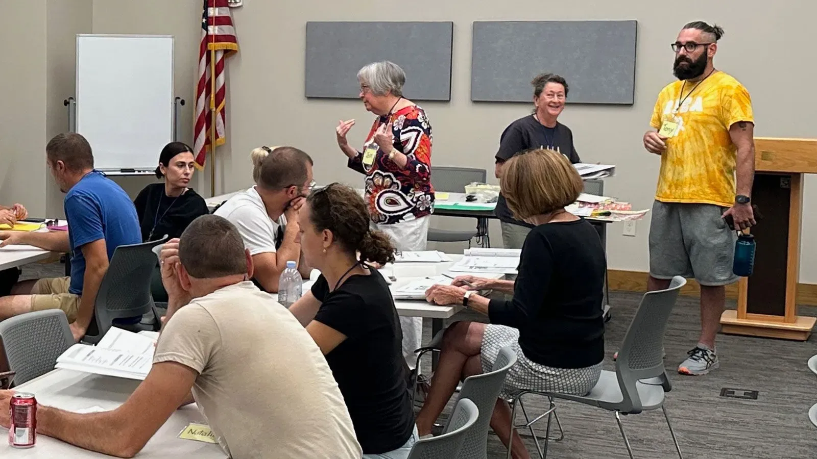 اجتماع لمجموعة من الأشخاص في قاعة، حيث يتحدث أحدهم بينما يتفاعل الآخرون. يركز النقاش على دعم اللاجئين الأوكرانيين في المجتمع.