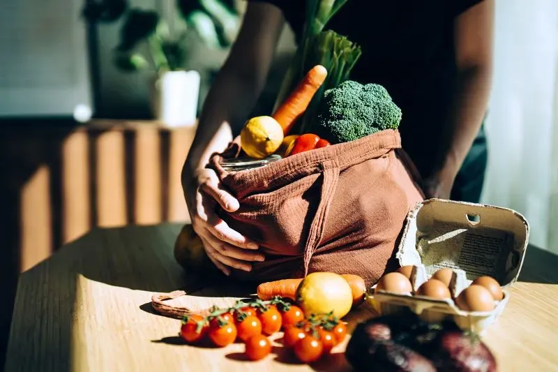 سلة تحتوي على مجموعة متنوعة من الخضروات والفواكه، مثل الجزر والبروكلي والطماطم، مع بيض وزيتون، تعكس أهمية التغذية الصحية.