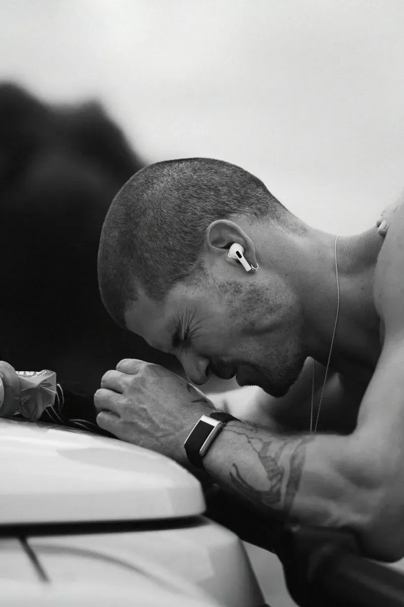 رياضي يتحمل، ويل غودج، يضع رأسه على سيارة بينما يستريح بعد جري طويل، مع تعبير عن التعب والإرهاق.