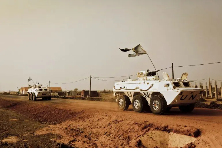 عربات مدرعة تابعة للأمم المتحدة تسير على طريق ترابي في منطقة كادوقلي بالسودان، في سياق جهود حفظ السلام amid ongoing conflict.