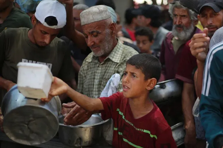 طفل فلسطيني يحمل وعاءً في طابور للحصول على الطعام وسط حشد من الناس في غزة، يعكس المعاناة الإنسانية نتيجة الصراع المستمر.