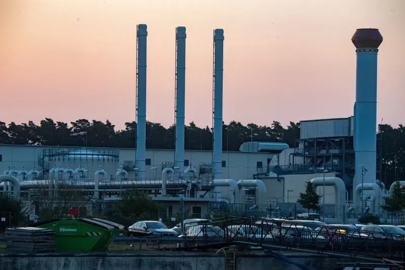 موقع منشأة تحتوي على أبراج أنابيب متصلة بتقنية طبيعية، مع وجود سيارات وحدود شجرية في الخلفية، في أفق غروب الشمس.