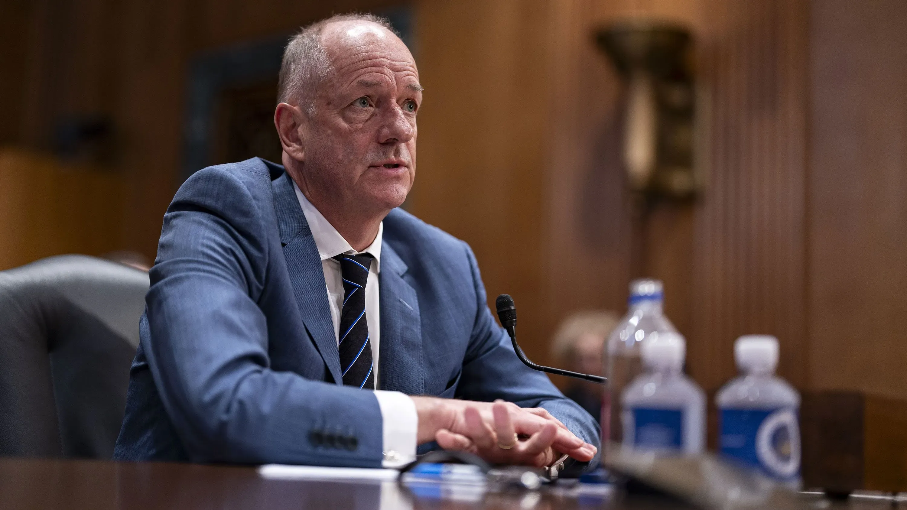 أندرو ويتي، الرئيس التنفيذي لمجموعة UnitedHealth Group، يتحدث في جلسة رسمية، مع زجاجات مياه على الطاولة، بعد إعلان تنحيه المفاجئ.