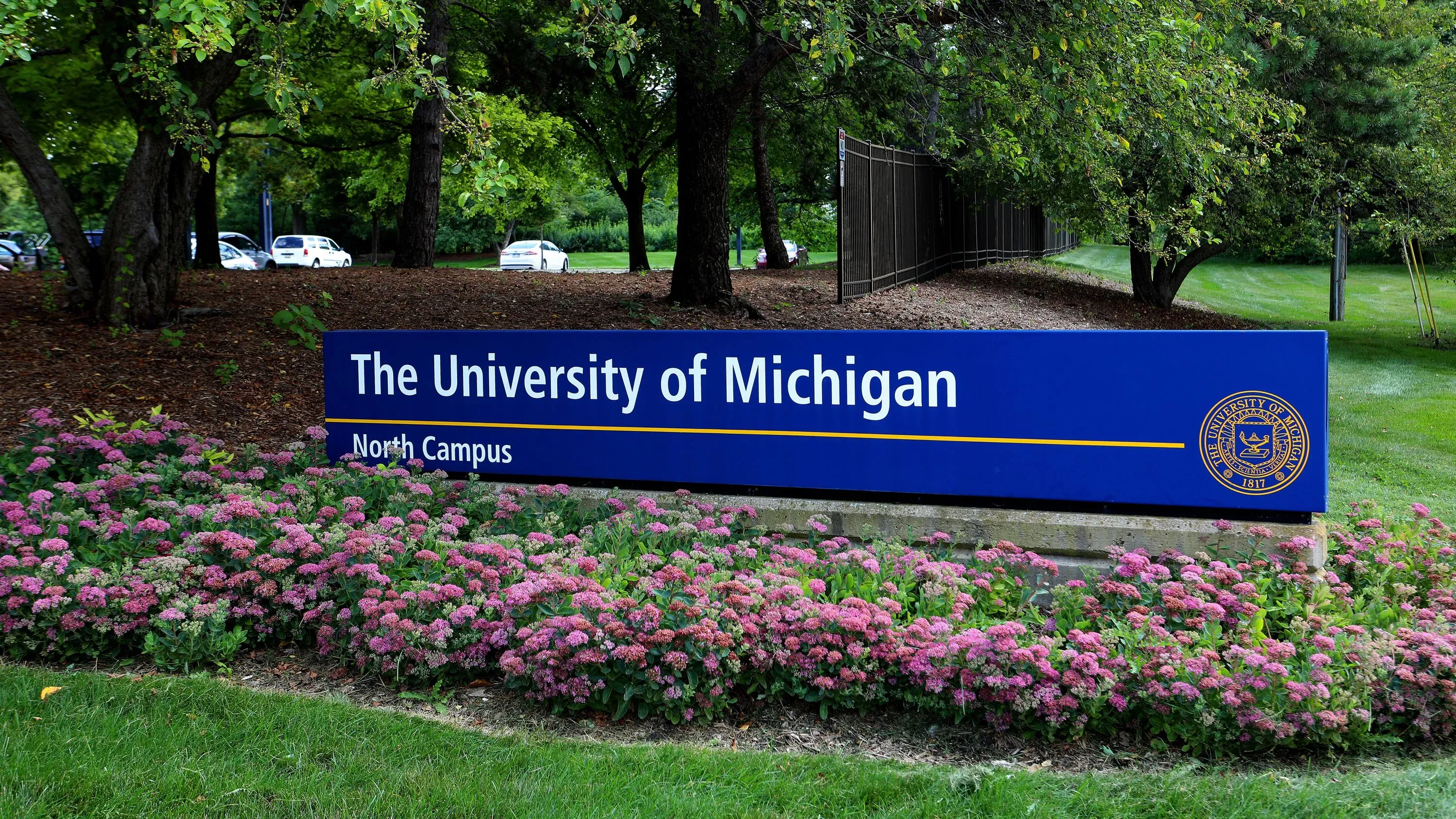 لافتة جامعة ميشيغان في الحرم الشمالي، محاطة بأزهار ملونة، تعكس التغييرات في برامج التنوع والمساواة التي تم الإعلان عنها مؤخرًا.