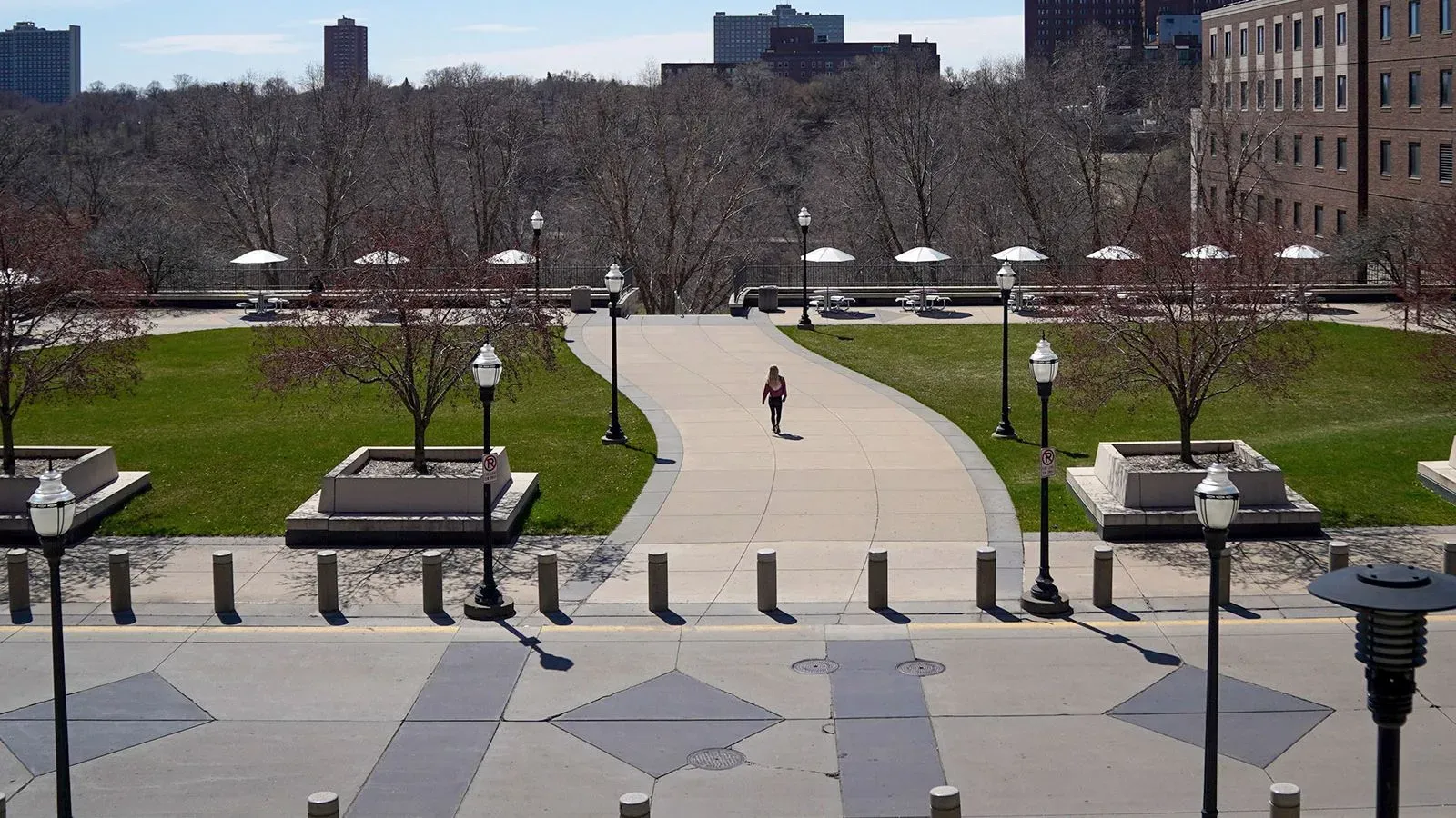 امرأة تسير بمفردها في حرم جامعة مينيسوتا، حيث تظهر الأشجار والأضواء في الخلفية، مما يعكس أجواء الدراسة والهدوء.
