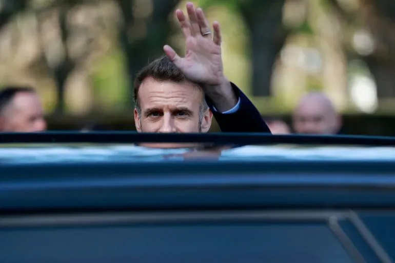 رئيس فرنسا إيمانويل ماكرون يلوح بيده من نافذة سيارة، وسط أجواء انتخابية في باريس، مع التركيز على الانتخابات المحلية.