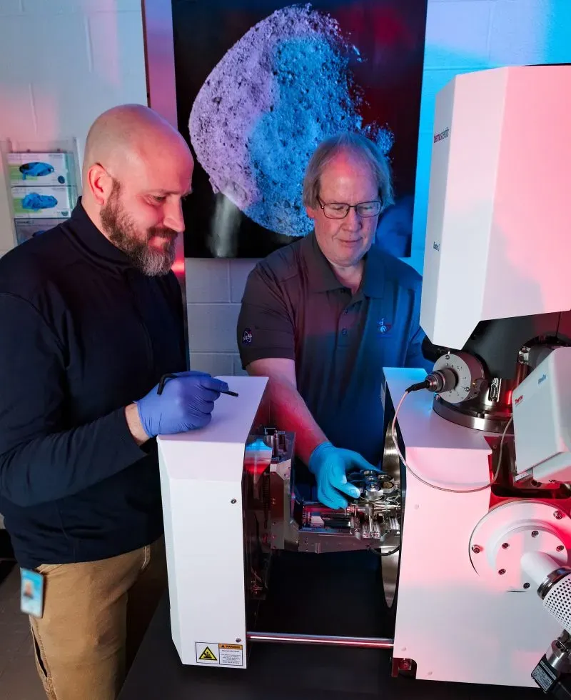 علماء يقومون بتحليل عينات كويكب بينو باستخدام معدات مختبرية، مع ظهور خلفية تخيلية للكويكب.