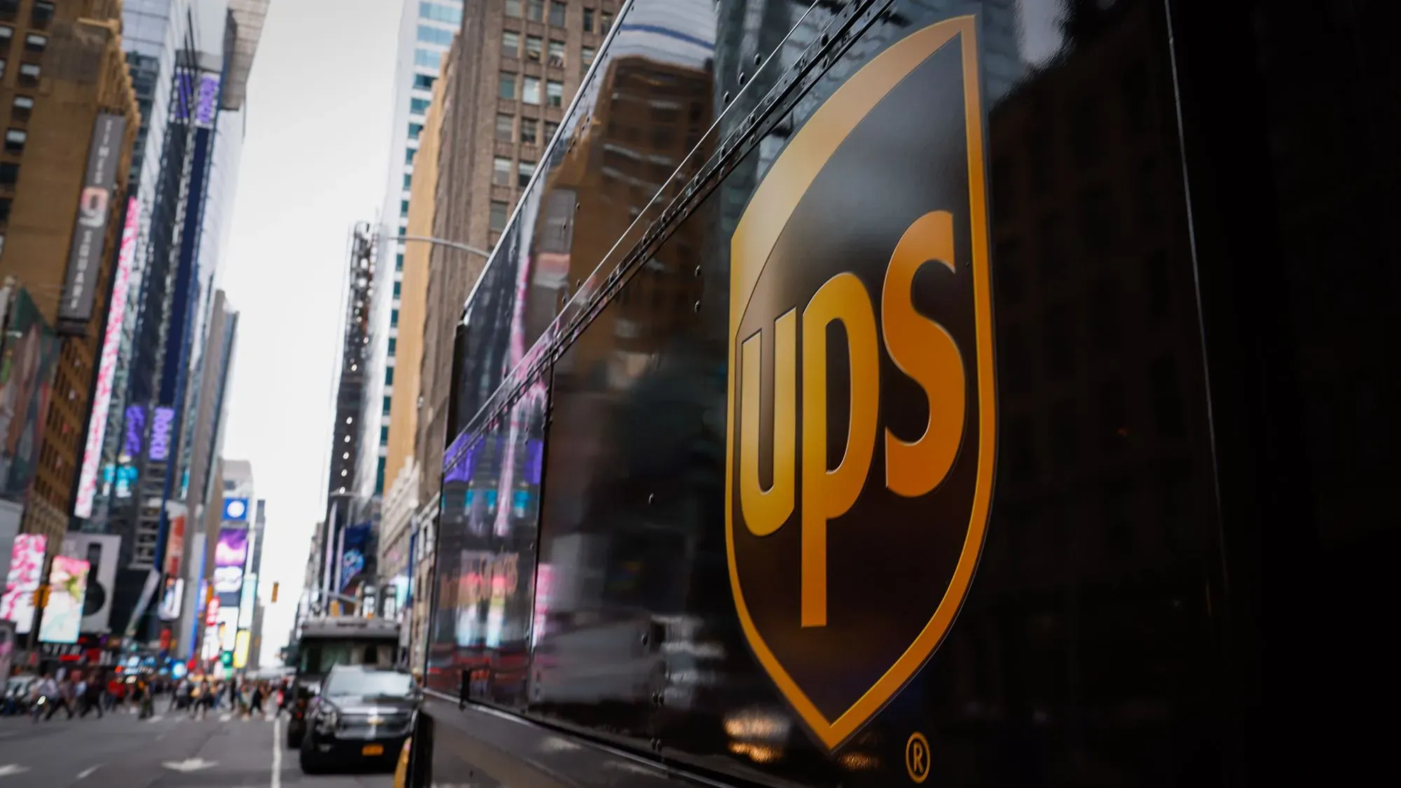شعار شركة UPS يظهر على شاحنة في مدينة مزدحمة، مع خلفية من المباني العالية، مما يعكس التحديات التي تواجهها الشركة في السوق.
