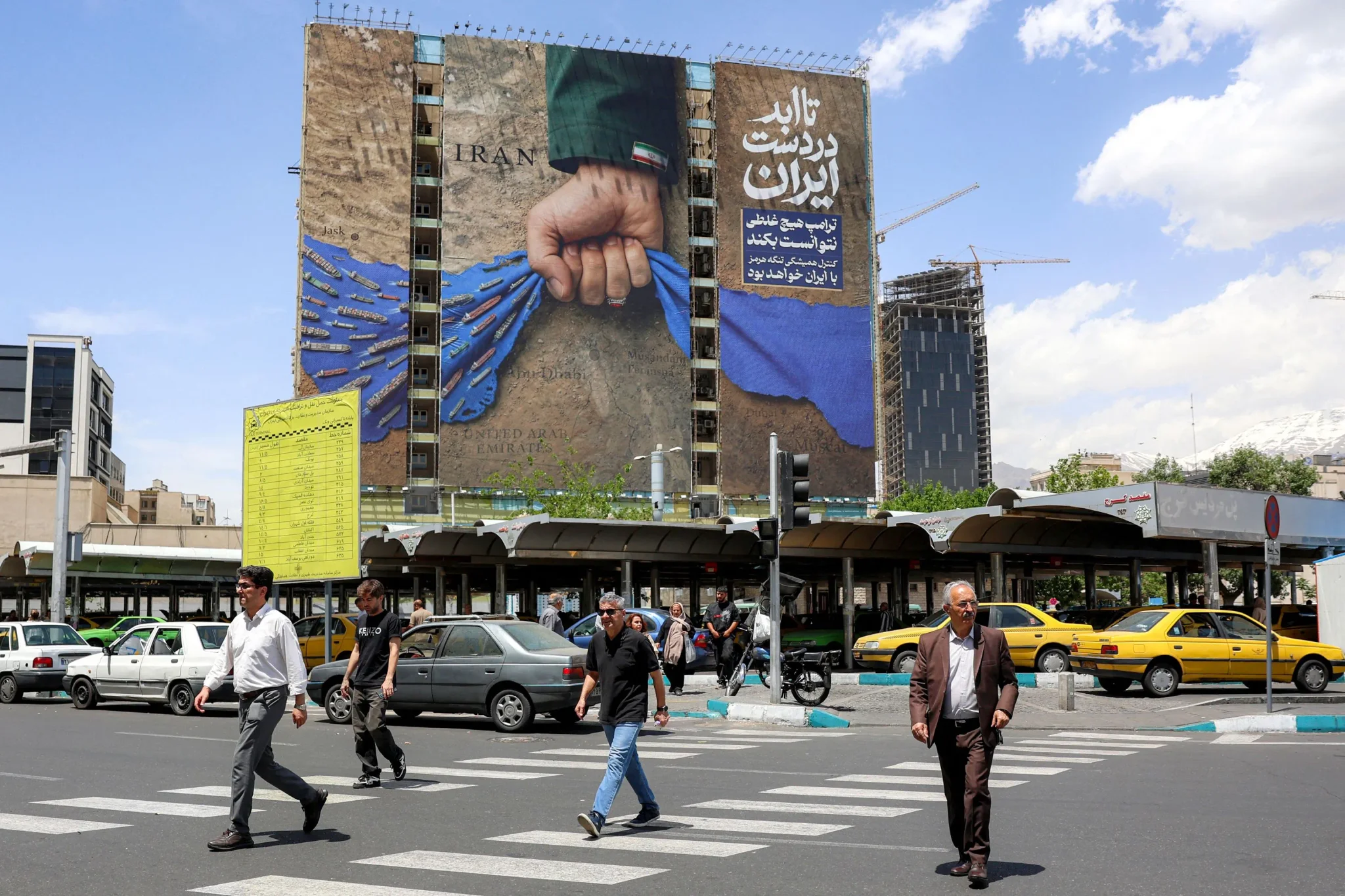لوحة جدارية في طهران تظهر يدًا تمسك بشريط أزرق، مع نصوص تدعو إلى الوحدة الإيرانية، بينما يمر الناس في الشارع.