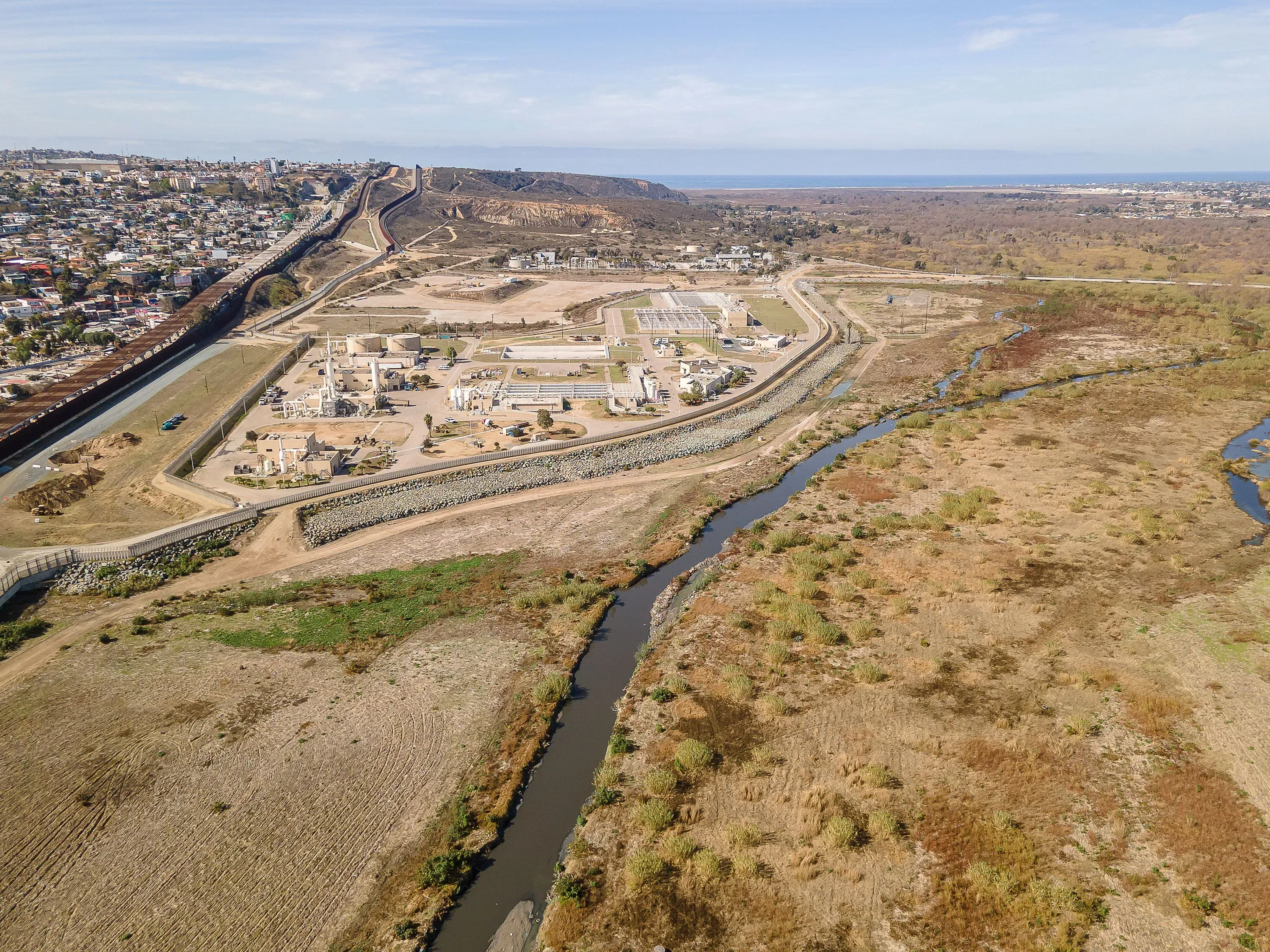 منظر جوي لمرافق معالجة مياه الصرف الصحي في حوض نهر تيخوانا، مع الحدود الفاصلة بين المكسيك والولايات المتحدة في الخلفية.