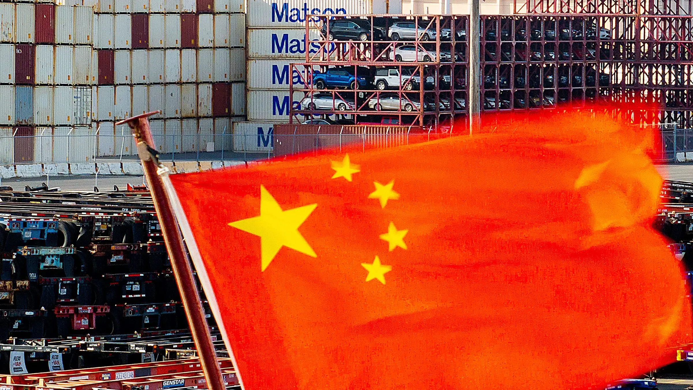 علم الصين يرفرف أمام حاويات شحن في ميناء، مما يعكس التوترات التجارية المتزايدة مع الولايات المتحدة بسبب الرسوم الجديدة على السفن الصينية.