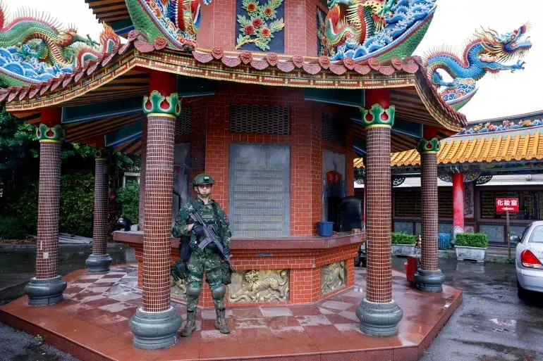 جندي تايواني مسلح يقف أمام معبد مزخرف بألوان زاهية، في سياق تعزيز الدفاعات الوطنية وسط التوترات مع الصين.