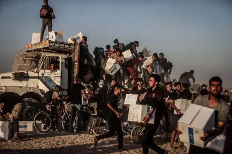 مشهد لمجموعة من الفلسطينيين يتجمعون حول شاحنة توصيل المساعدات في غزة، حيث يحملون صناديق الطعام وسط ظروف صعبة.