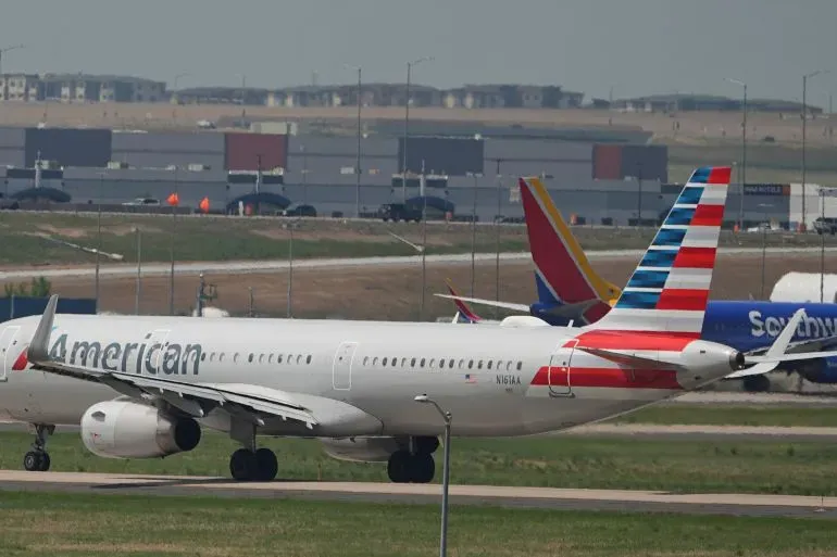 طائرة أمريكية تابعة لشركة الطيران الأمريكية، متوقفة على مدرج في مطار، مع وجود طائرات أخرى في الخلفية، تعكس تأثير الصراع على حركة الطيران في الشرق الأوسط.