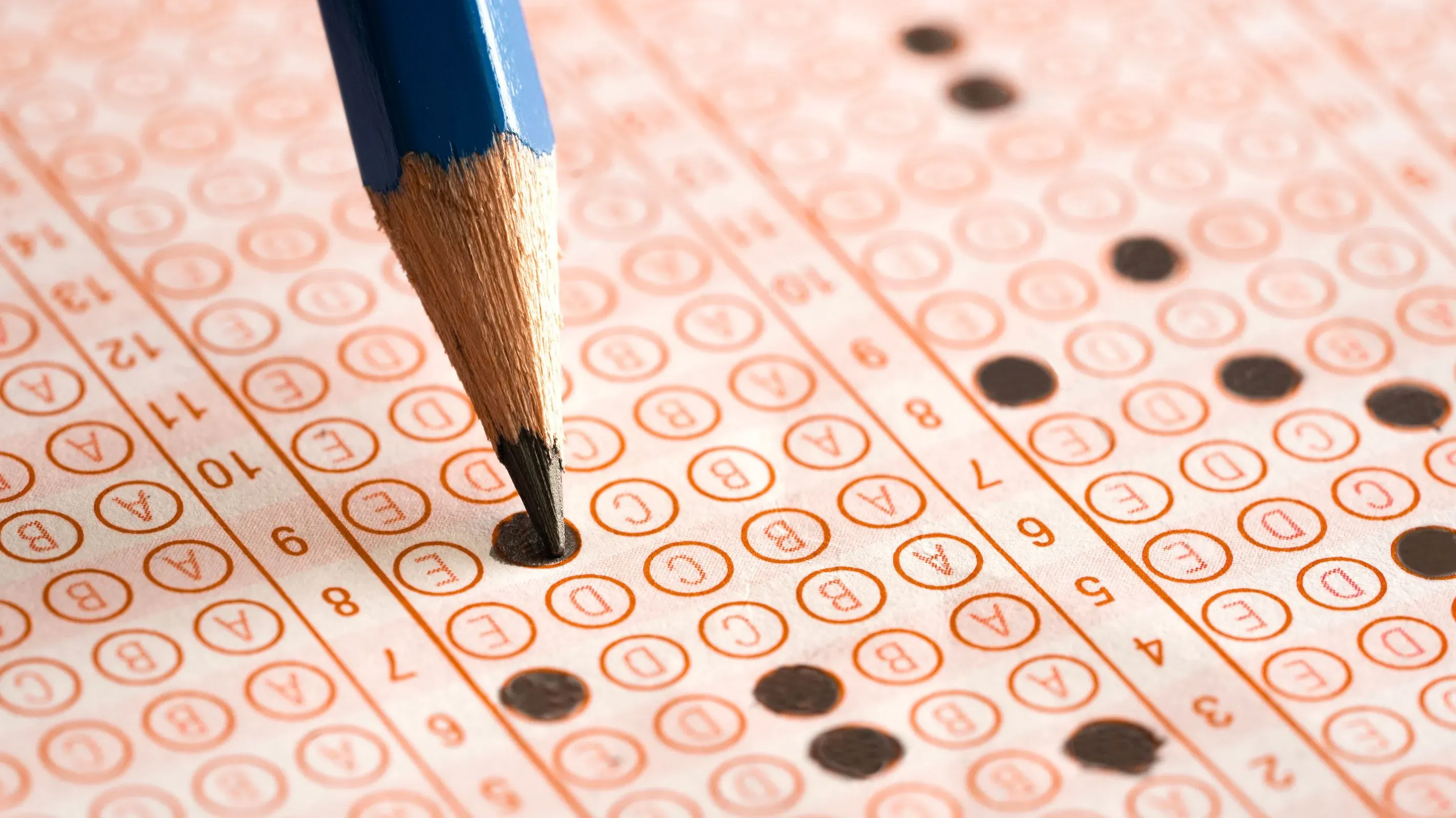 قلم رصاص أزرق ينقط على ورقة اختبار مُعدة لطلاب الصفين الرابع والثامن، تظهر علامات الاختيار في مختلف الدوائر، تعكس نتائج امتحانات القراءة والرياضيات في أمريكا.