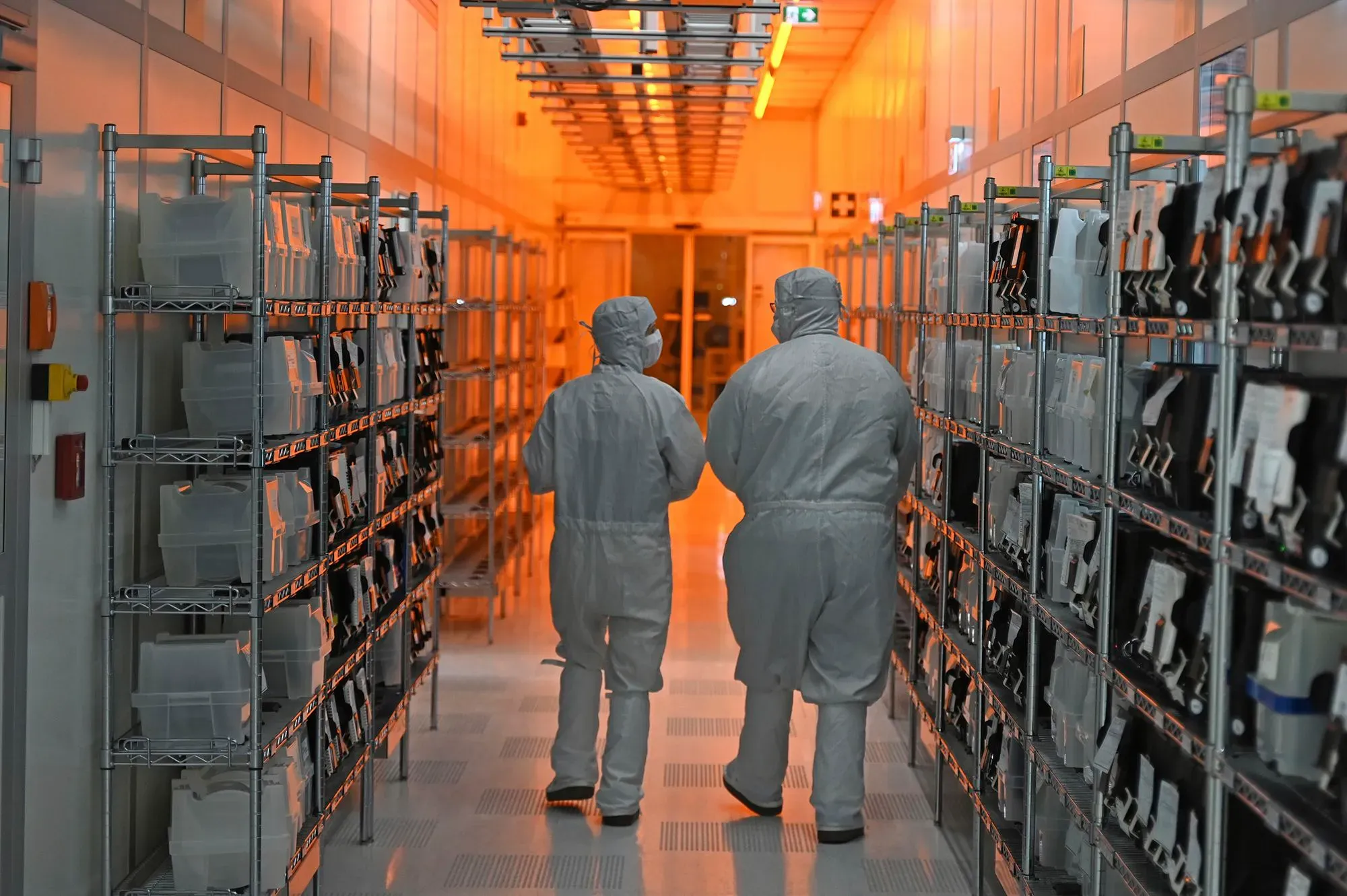 ممر في مصنع نيكسبيريا حيث يرتدي العاملون ملابس واقية، مع رفوف تحتوي على مكونات إلكترونية ضرورية لصناعة السيارات.