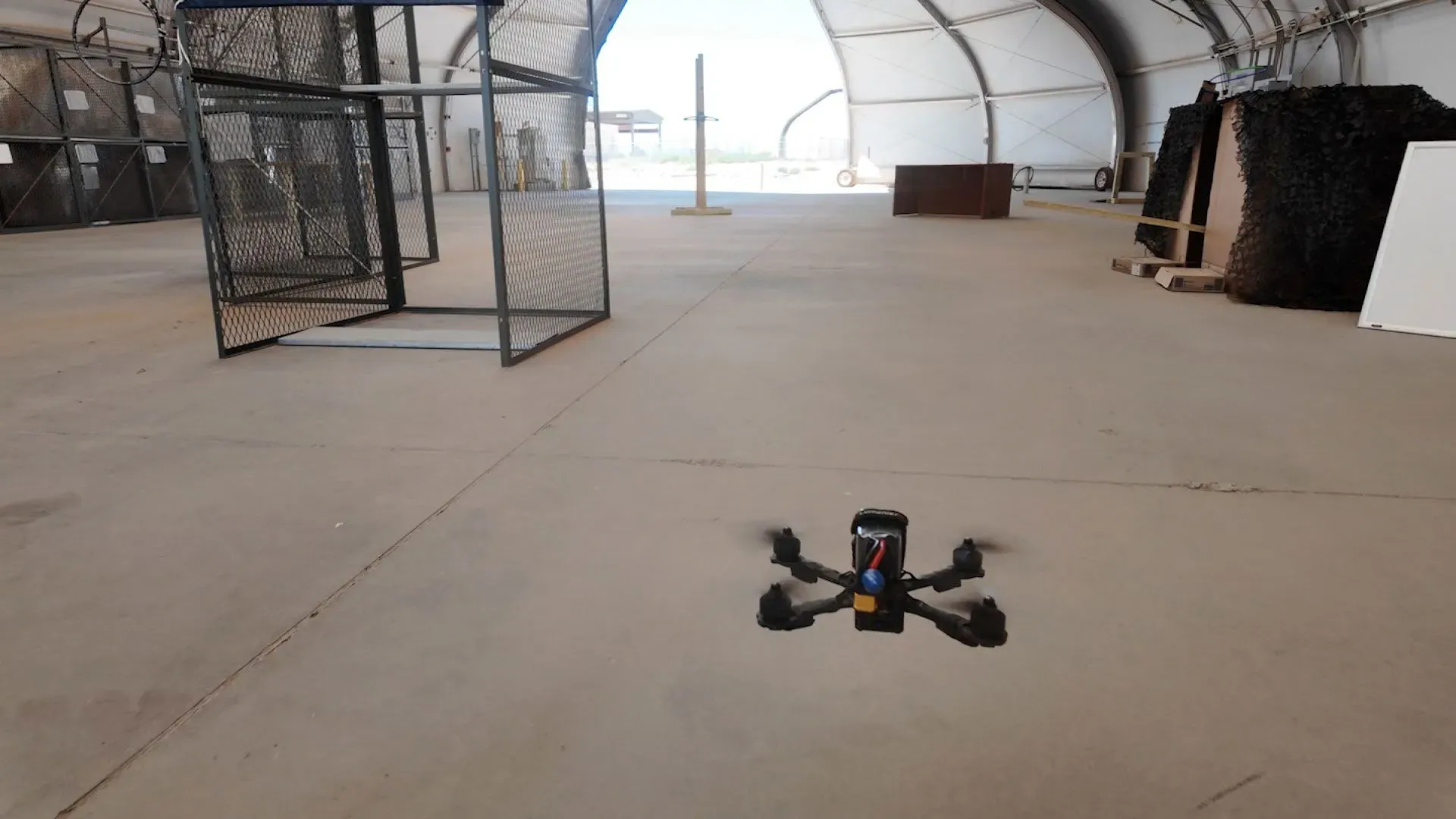 طائرة بدون طيار صغيرة تحلق داخل قاعدة عسكرية، مع وجود حواجز تدريبية في الخلفية، تعكس جهود الجيش الأمريكي في استخدام التكنولوجيا الحديثة في الحروب.