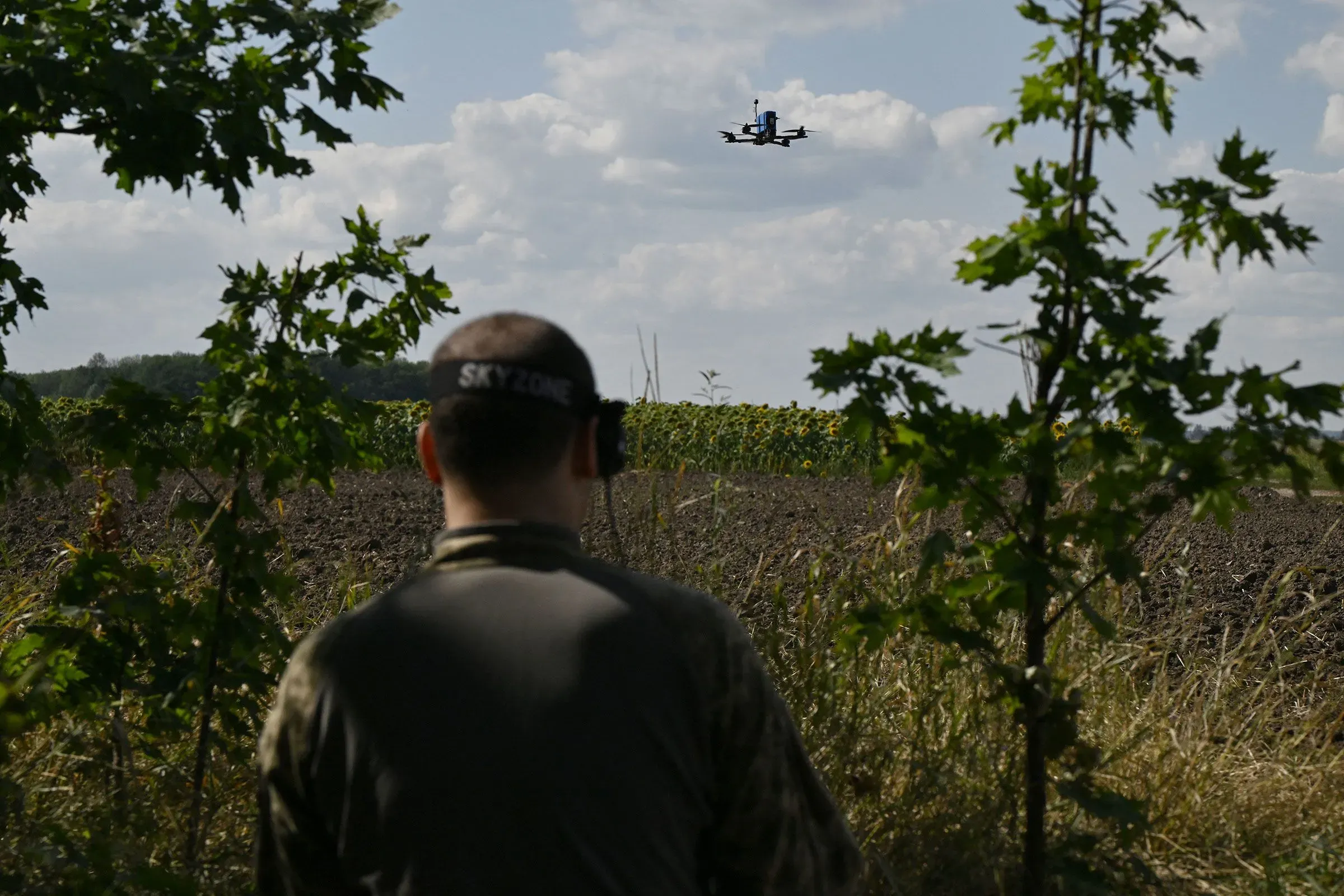جندي يتابع طائرة مسيرة صغيرة في حقل، مما يبرز استخدام التكنولوجيا الحديثة في العمليات العسكرية.