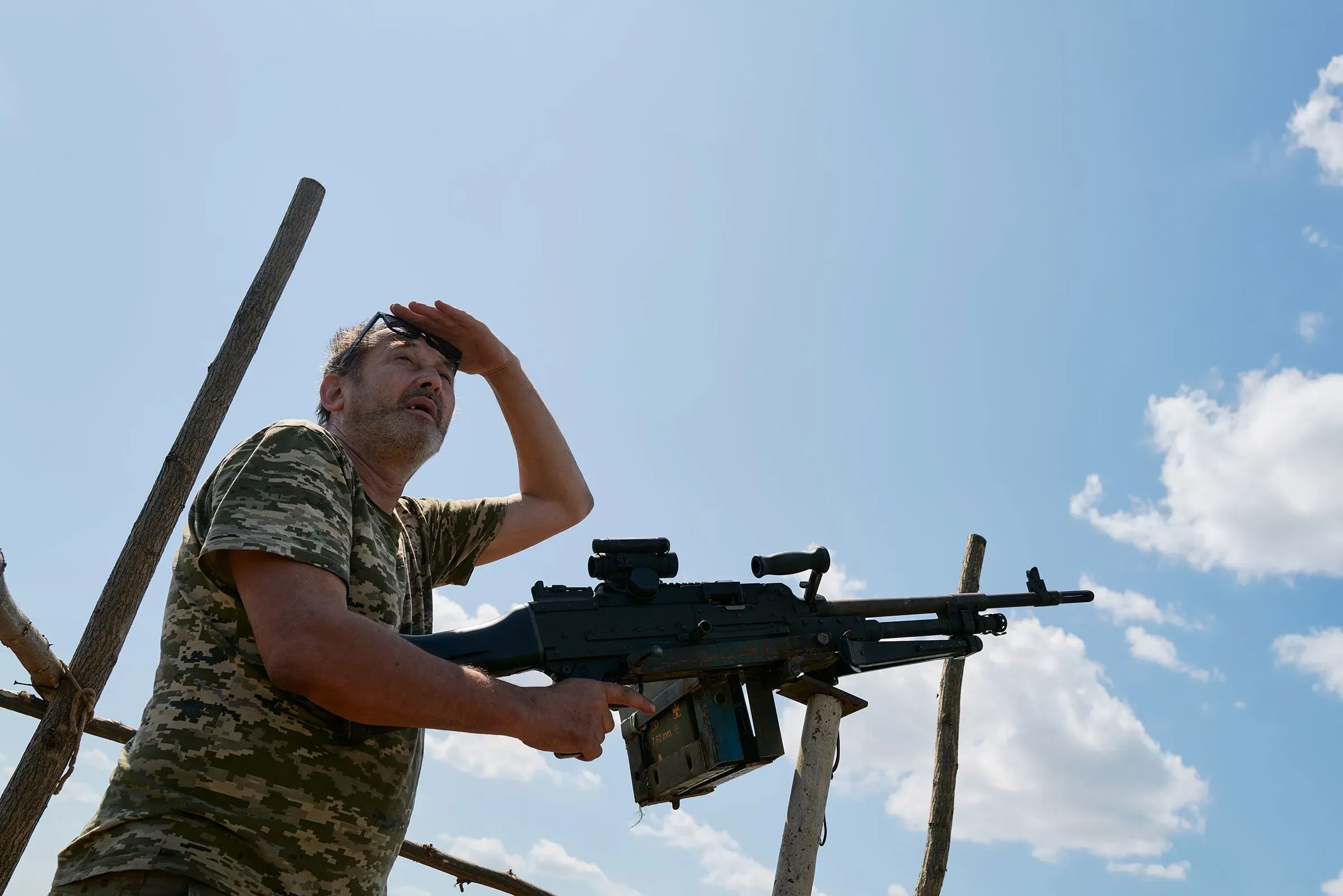 رجل يرتدي زيًا عسكريًا ينظر إلى السماء بقلق، ممسكًا بسلاحه، في سياق الحرب الحديثة والتطورات في استخدام الطائرات بدون طيار.