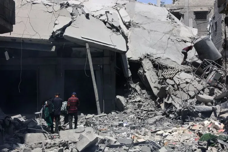 دمار هائل في مبنى نتيجة القصف، مع أشخاص يتجولون بين الأنقاض في منطقة متضررة، مما يعكس آثار الصراع في غزة.